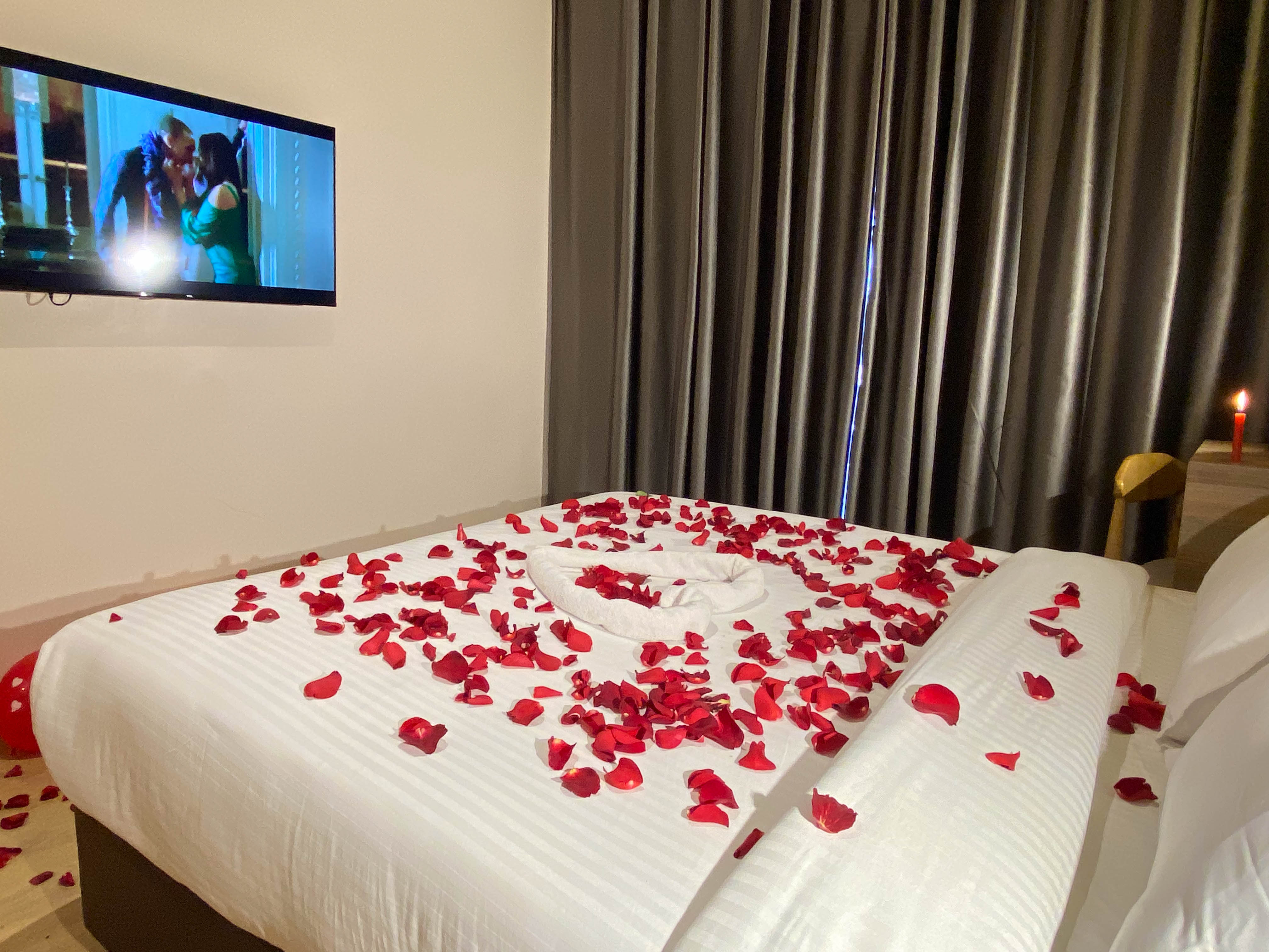 Rose petals scattered around a towel heart on crisp white bedding