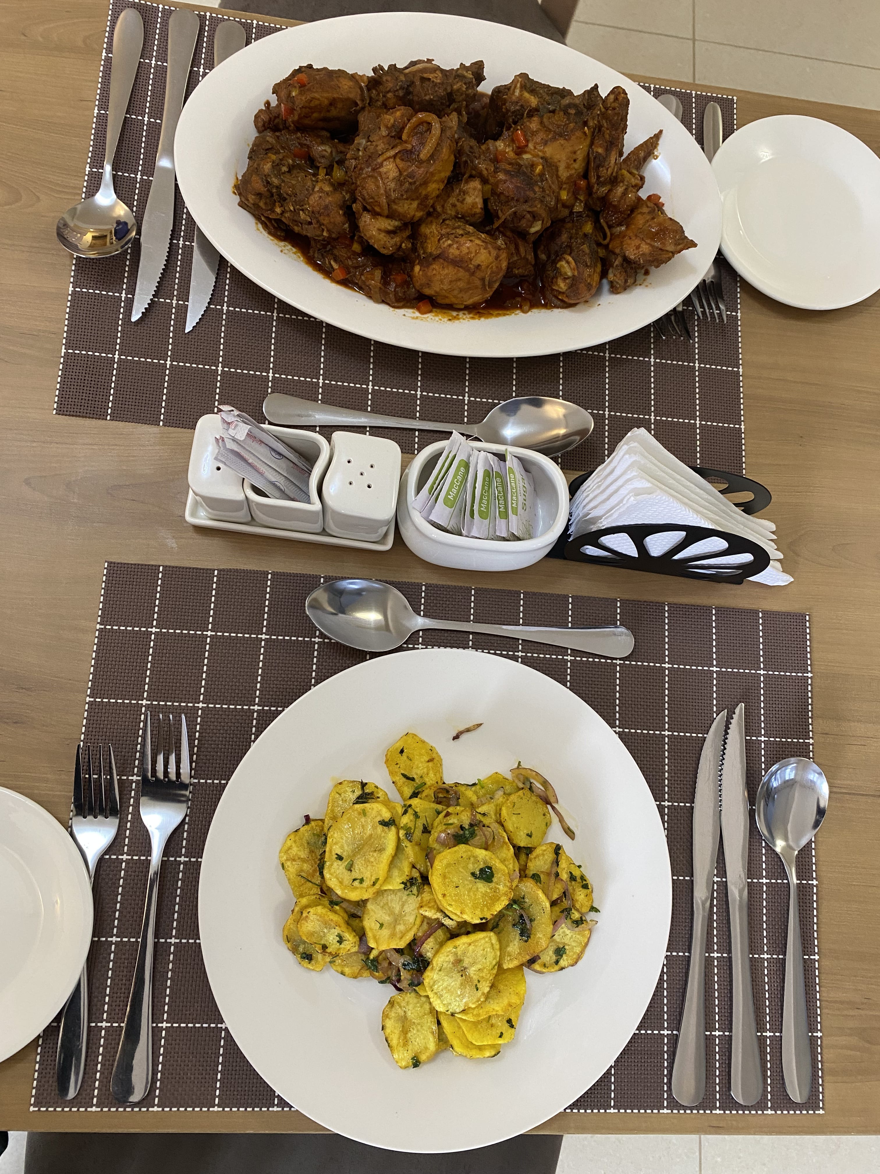 A set table with chicken wet fry, spiced potato rounds and condiments on woven placemats