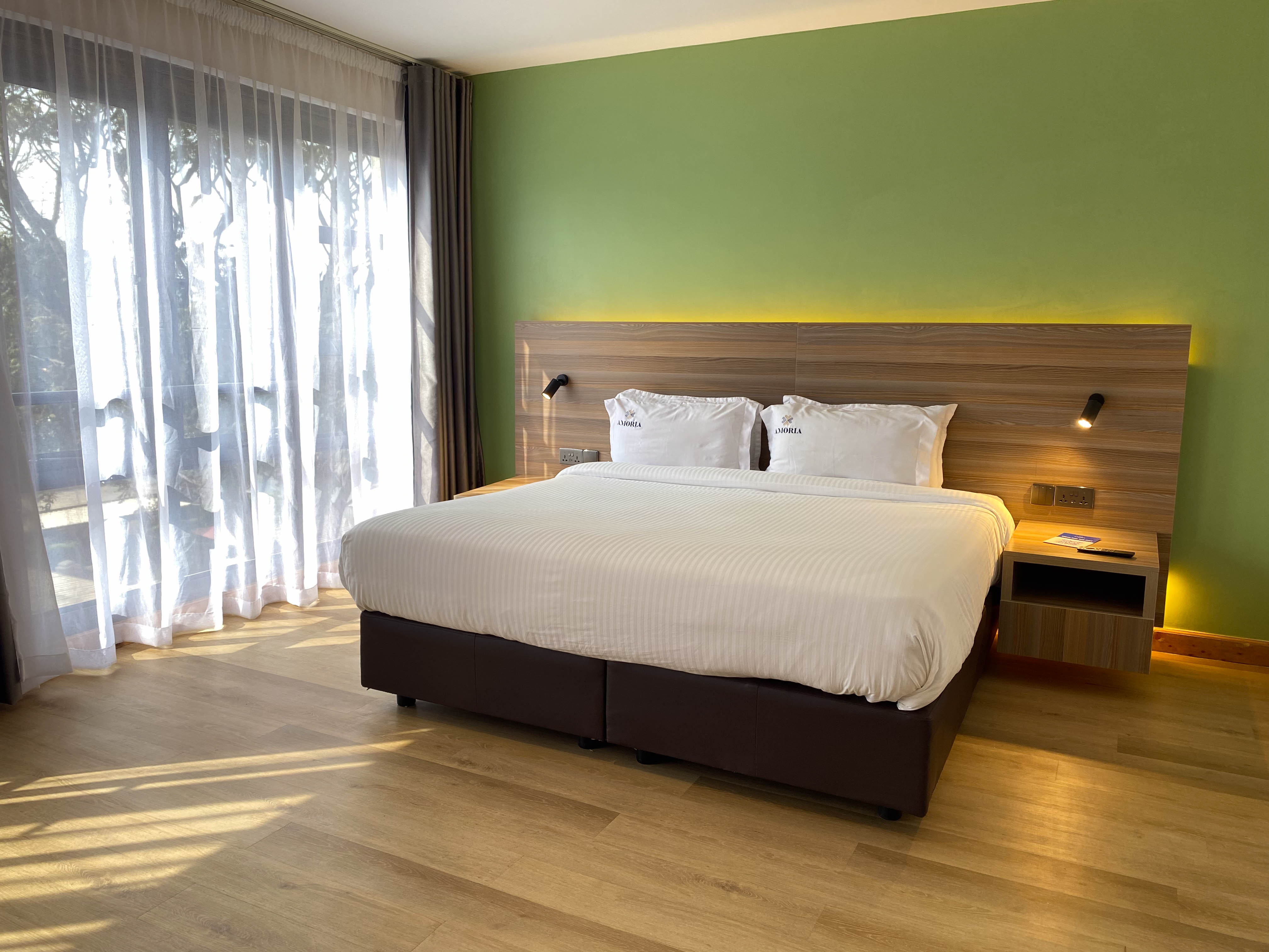 The Executive room's king bed against a green feature wall, evening sun through the balcony sheers